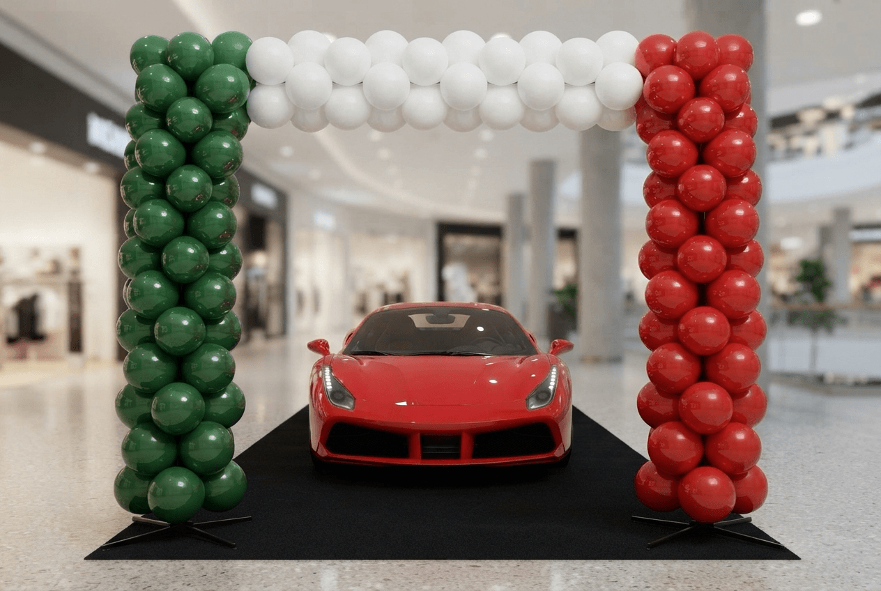 Colonnes de ballons en vert, blanc et rouge surmontées d’une arche, autour d’une voiture de sport rouge dans le showroom