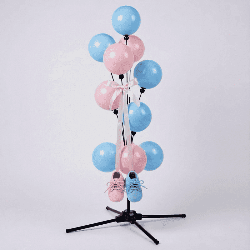 Adorable fontaine de ballons de révélation de sexe avec des chaussons de bébé roses et bleus suspendus à des rubans dorés entre les ballons
